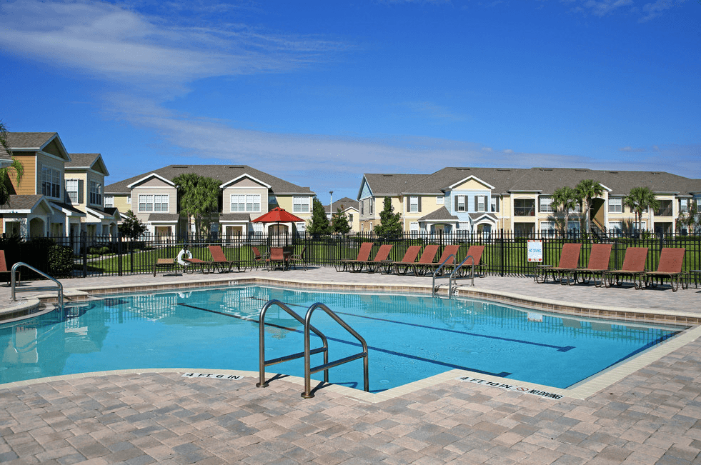 a swimming pool with red chairs and houses in the background