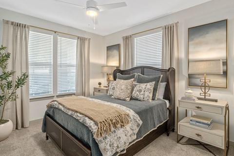 A bedroom with a large bed, a ceiling fan, and a painting on the wall.