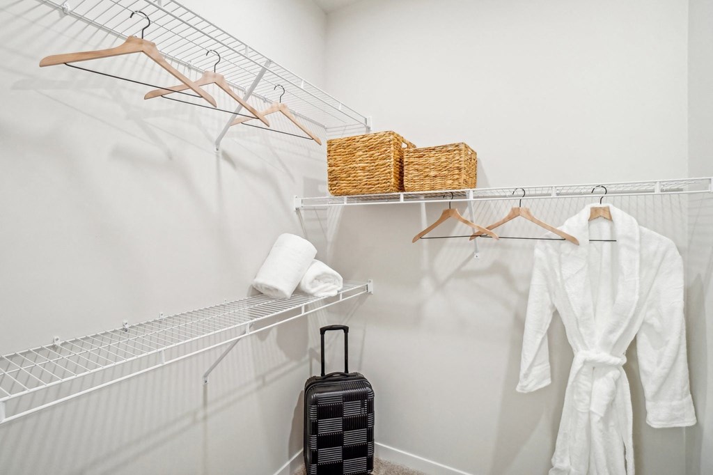 a walk in closet with a white robe and accessories and a suitcase