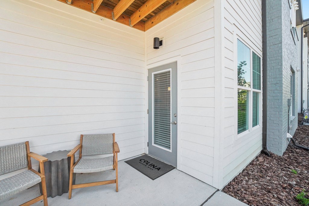 the front porch of a white house with two chairs and a door