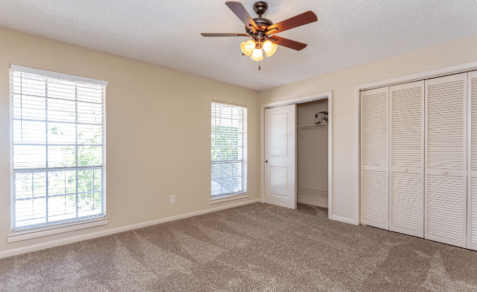 an empty living room with a ceiling fan and a closet