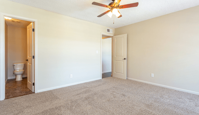 an empty living room with a ceiling fan and a toilet