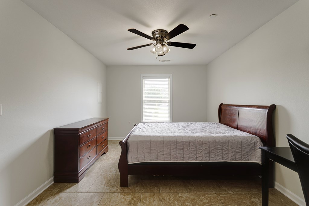 A bedroom with a bed, dresser, and ceiling fan.