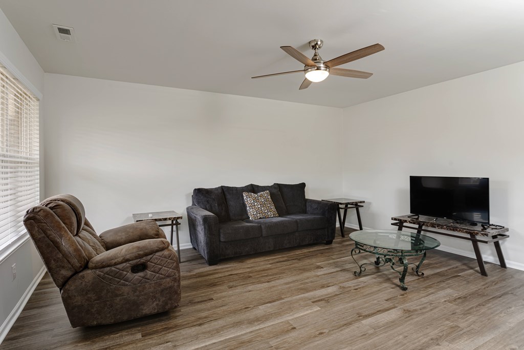 A living room with a brown chair, grey couch, and a glass coffee table.