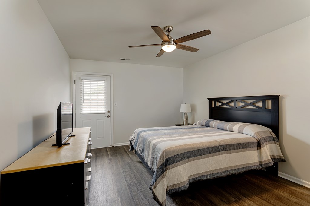 A bedroom with a bed, a television, and a ceiling fan.