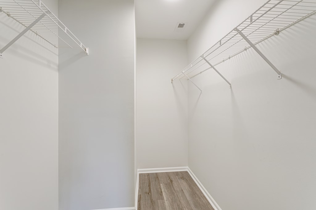 A walk in closet with white walls and wood flooring.
