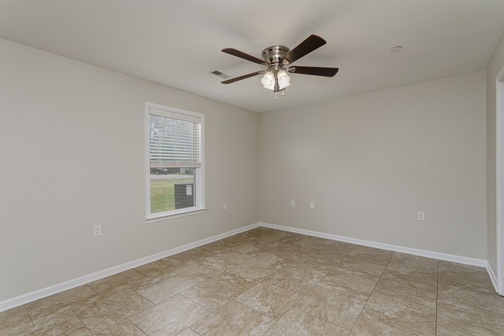 A room with a ceiling fan and a window showing a view of a lawn and a house.