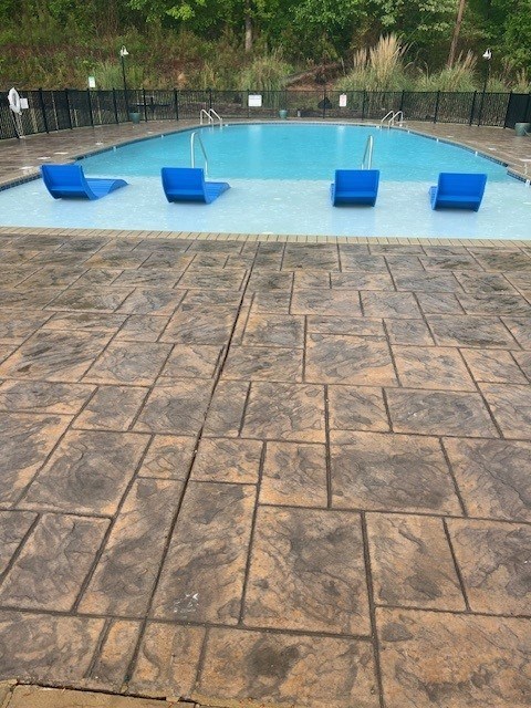 A pool surrounded by blue chairs and a black fence.