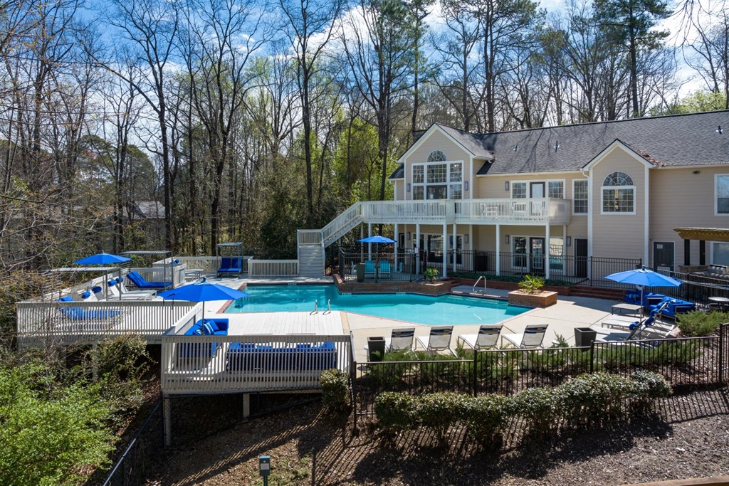 Large outdoor pool surrounded by trees, lounge chairs and umbrellas with staircase access to the clubhouse at Summerchase at Riverchase in Hoover, Alabama.