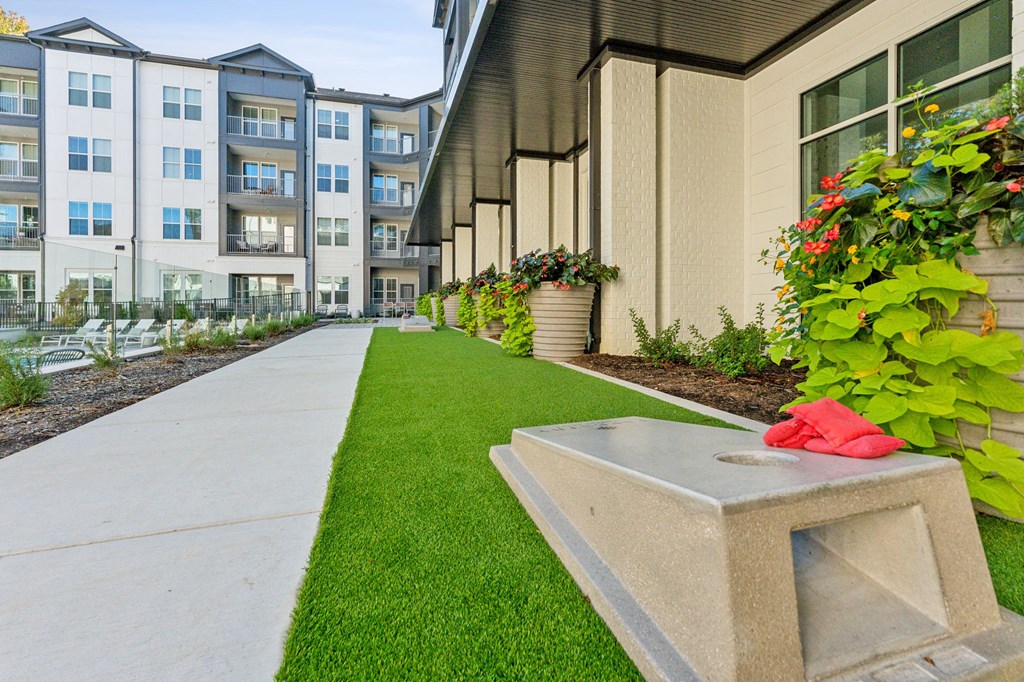 a sidewalk in front of an apartment building with grass and flowers
