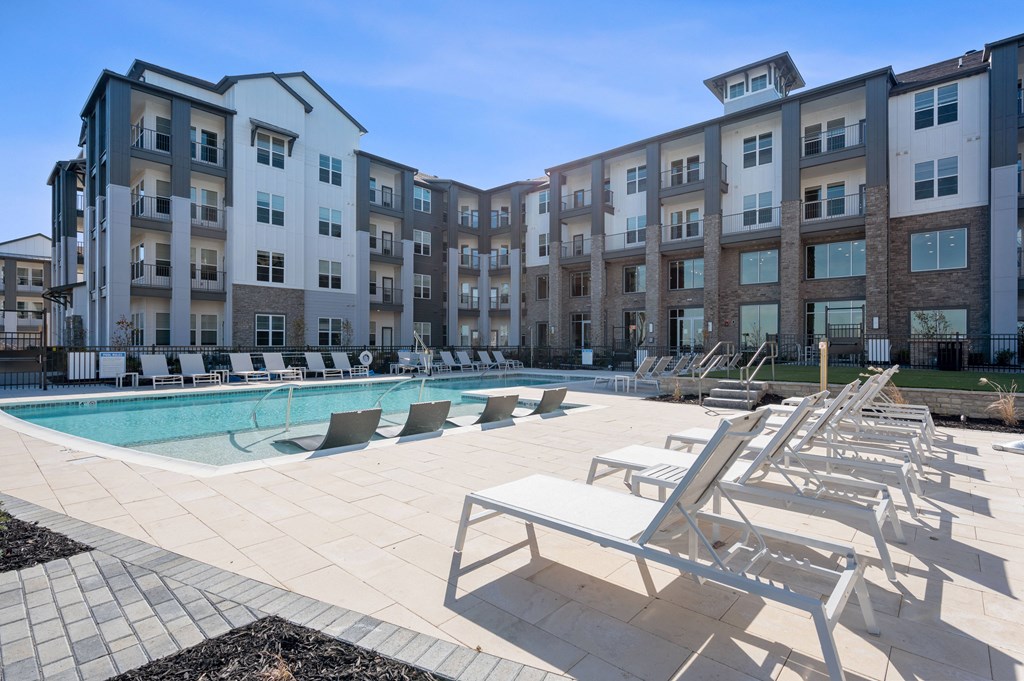 an outdoor pool with lounge chairs and an apartment building