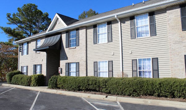 an apartment building with shrubs in front of a parking lot