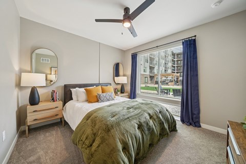 A bedroom with a bed, a ceiling fan, and a window with a view of a building outside.