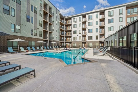 A swimming pool surrounded by apartment buildings and lounge chairs.