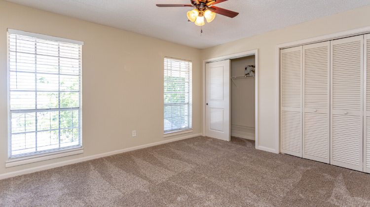 an empty living room with two windows and a ceiling fan
