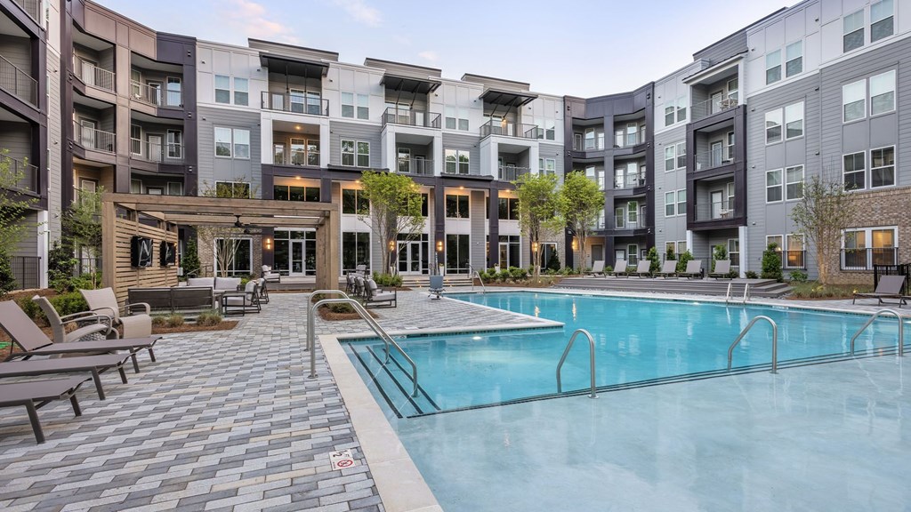 A large swimming pool surrounded by lounge chairs and apartment buildings.