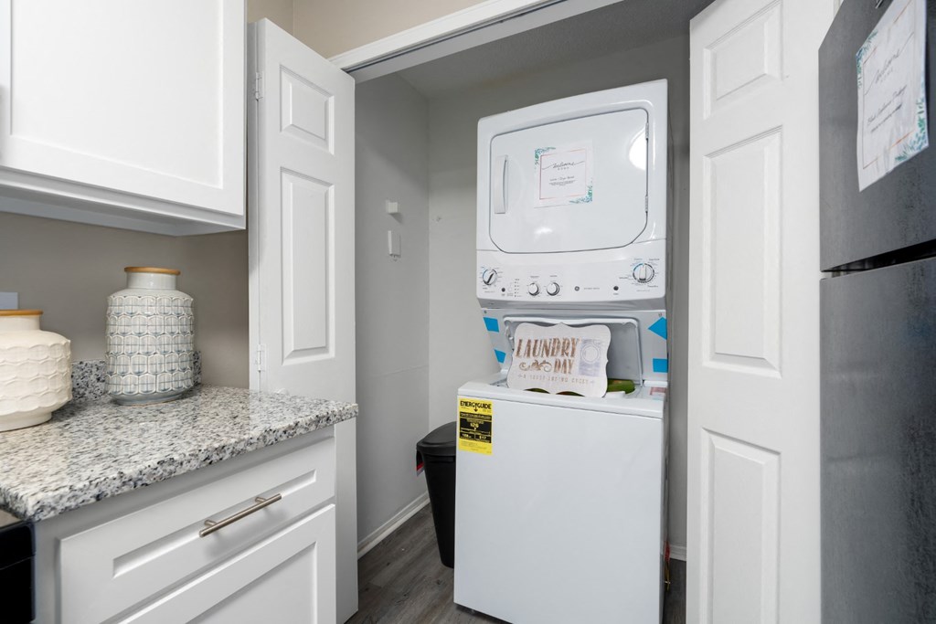 A kitchen with granite countertops, white cabinets, and a washer and dryer unit at Summerchase at Riverchase in Hoover, Alabama.