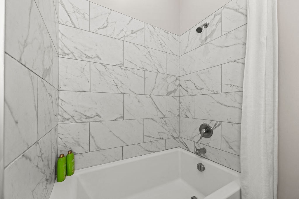 a white tiled bathroom with a tub and a shower curtain