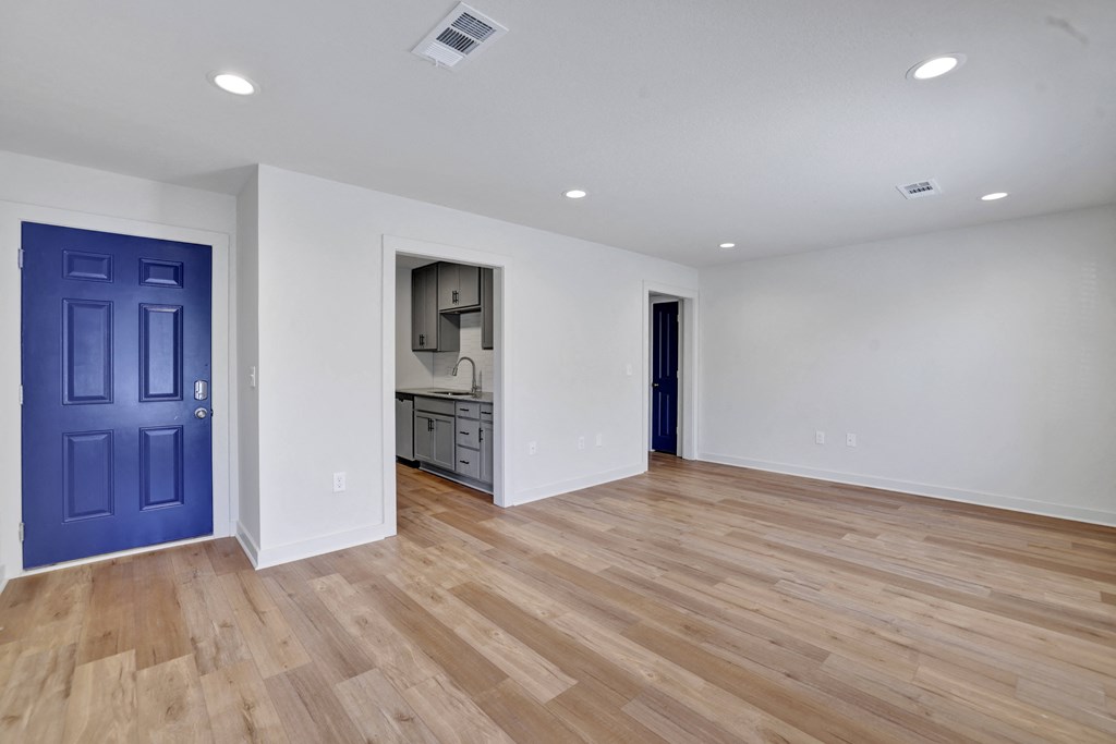 an empty living room with a blue door and a kitchen