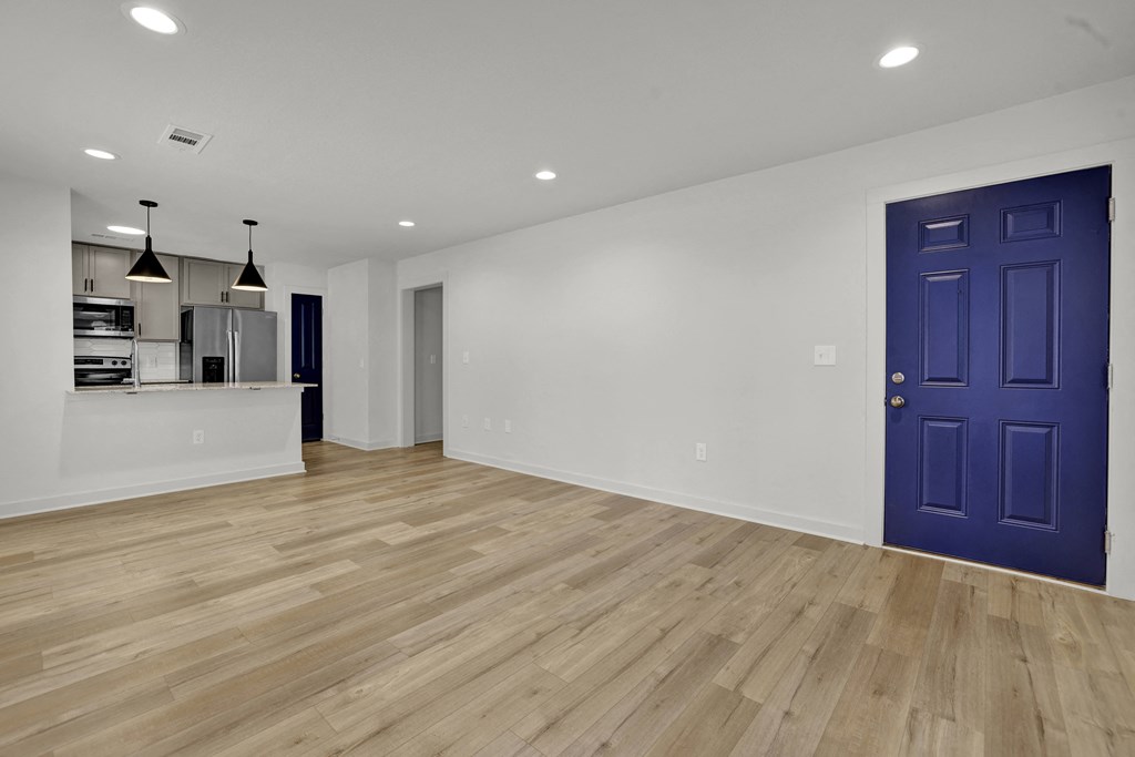 an empty living room with a blue door and a kitchen