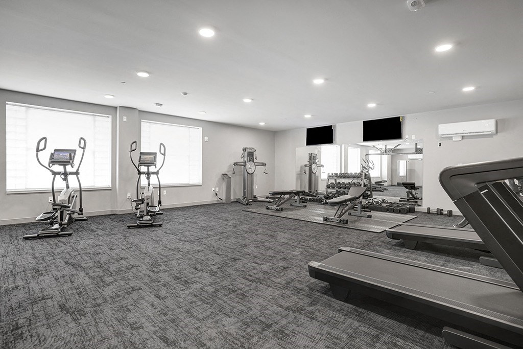 a gym with treadmills and other exercise equipment in a room with windows