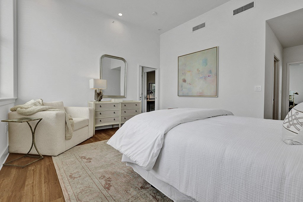 a white bedroom with a bed and a chair and a mirror