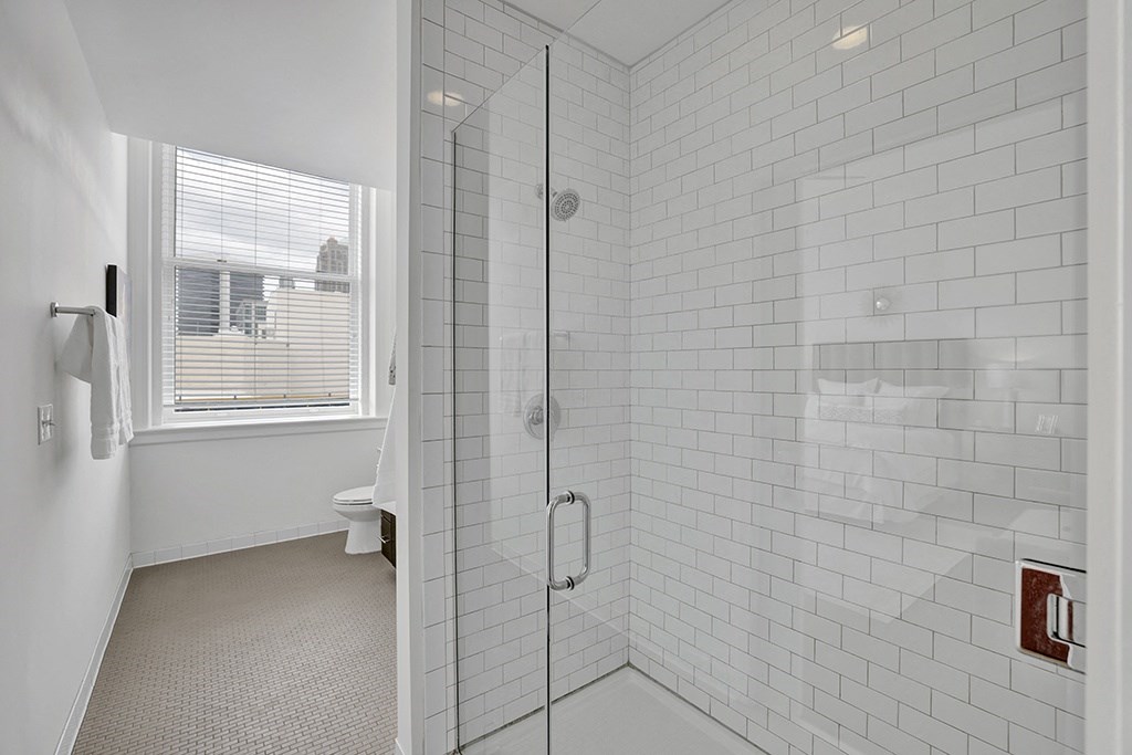 a white tiled bathroom with a shower and a window