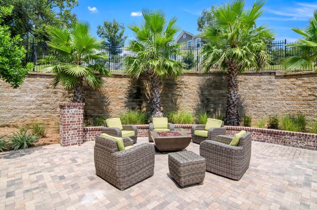 a patio with wicker furniture and a fire pit in front of a brick wall