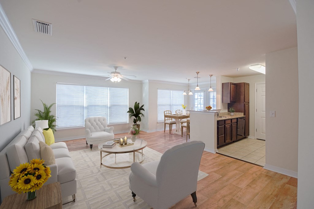 A living room with a grey sofa, a white chair and a coffee table with sunflowers on it at 10X Audubon Park apartments in Daphne, AL 