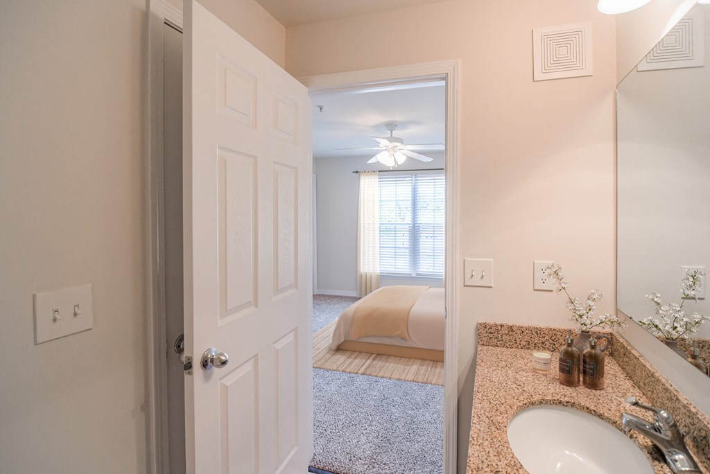 a bathroom with a sink and a bedroom in the background at 10X Audubon Park apartments in Daphne, AL 