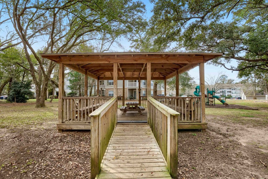 a small wooden bridge leading to a cabin with a playground in the background at 10X Audubon Park apartments in Daphne, AL 