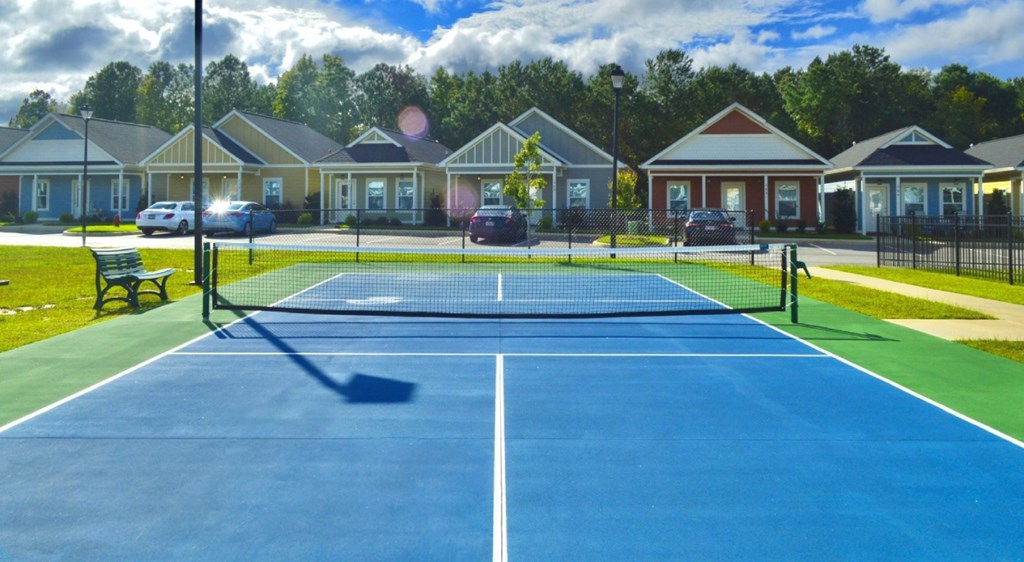 A blue tennis court in front of a row of houses.