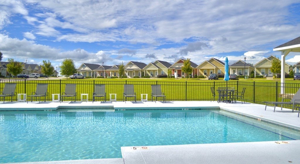 A swimming pool surrounded by a black fence and yellow chairs.