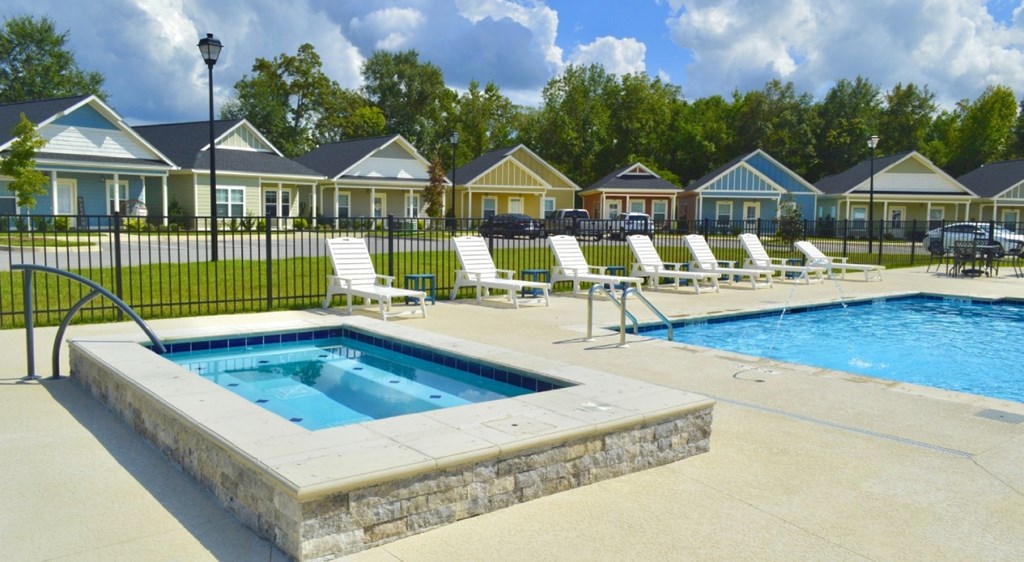 A pool surrounded by a stone wall and chairs.