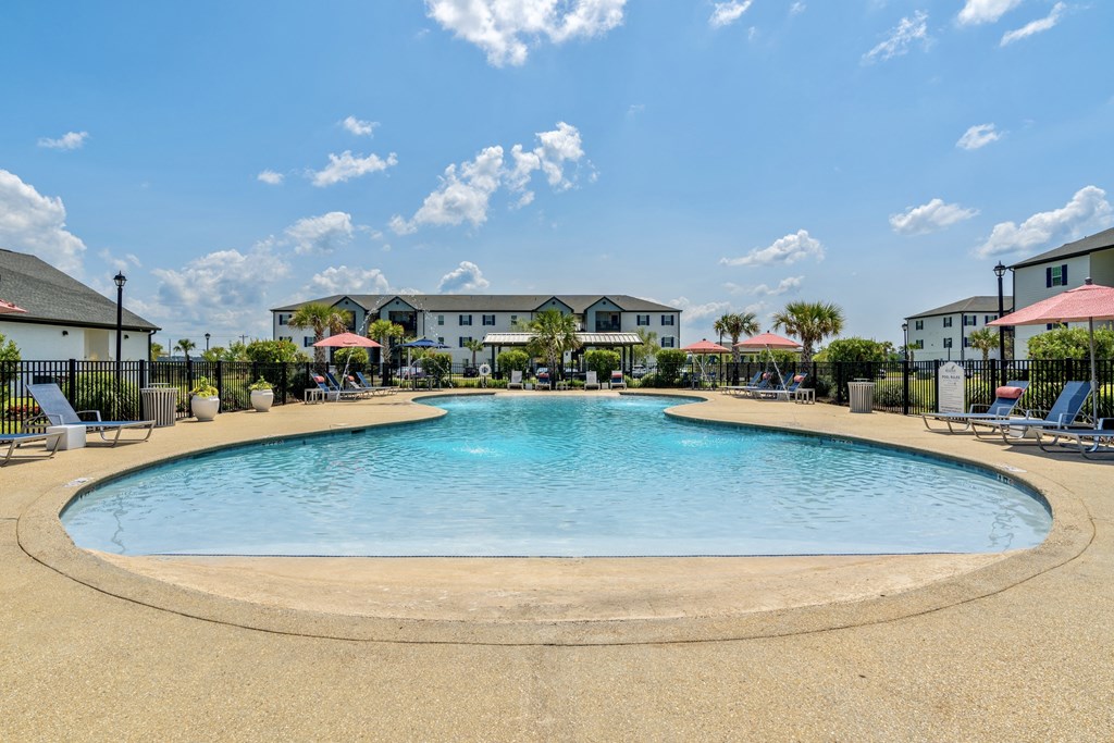 a resort style pool with lounge chairs and umbrellas at the whispering winds apartments in pear