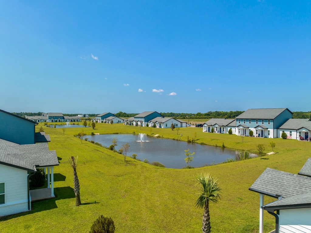a large grassy area with a pond in front of a row of houses