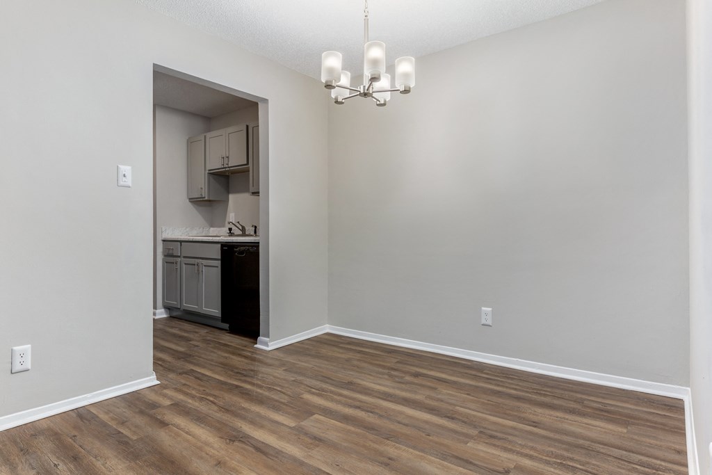 an empty living room with a kitchen in the background