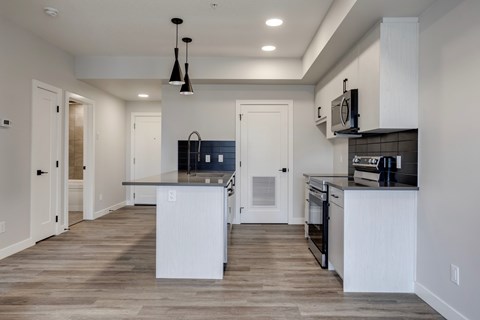 A modern kitchen with white cabinets and a wooden floor.