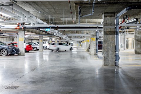 A parking garage with cars parked and a green sign above them.