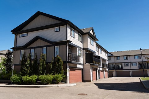 A large, modern two-story residential building with a parking lot in front.