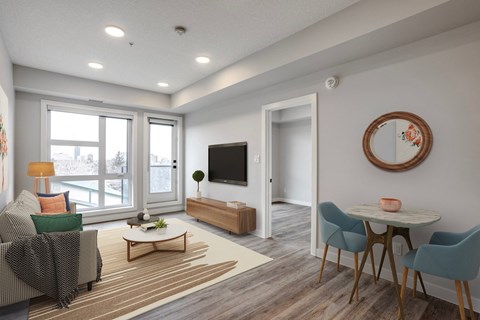 A living room with a grey couch, a wooden coffee table, a flat screen TV, and a round mirror on the wall.