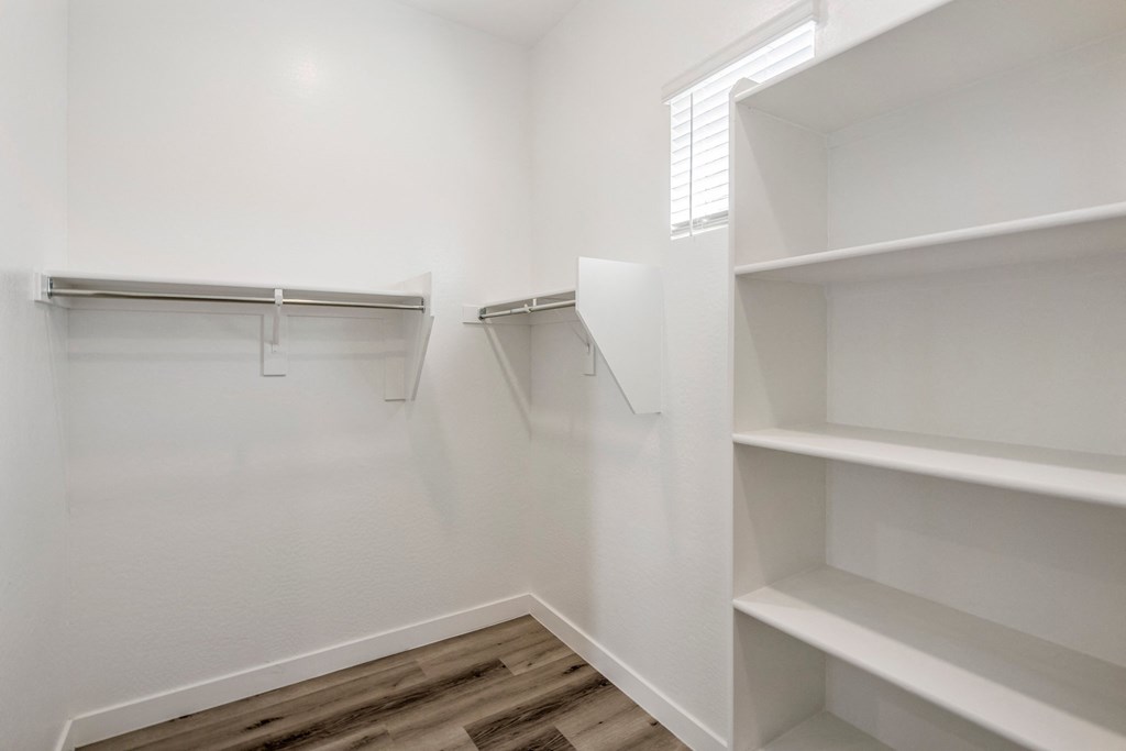 a spacious walk in closet with white walls and wood flooring
