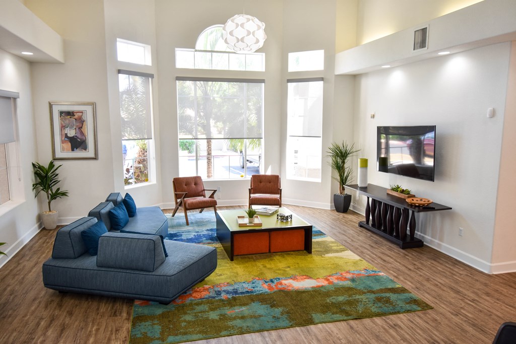 Clubhouse seating area with navy blue sofas, Coffee table, and mounted television on wall.  large picture windows providing a natural light within the room