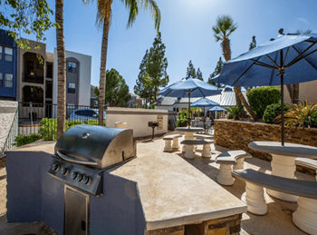 a bbq grill in a courtyard with tables and umbrellas at Enclave at Paradise Valley in Phoenix, AZ 85032