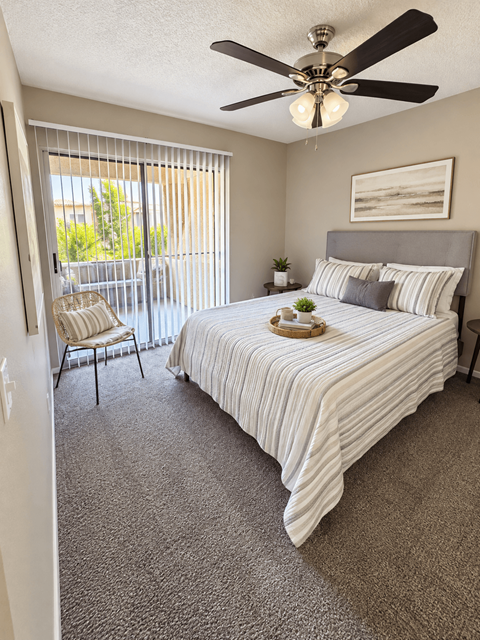 A bedroom with a bed, chair, and window with blinds.