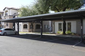 A white car is parked under a covered parking structure.