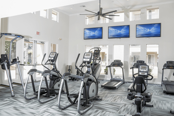 A gym with a variety of exercise equipment including treadmills, stationary bikes, and elliptical machines.