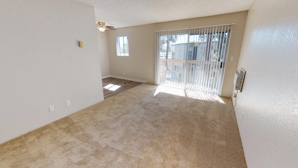 an empty living room with a sliding glass door to a balcony