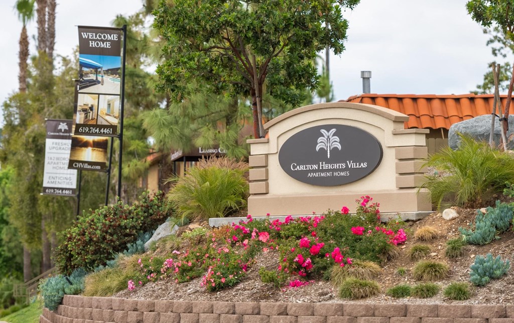 Sign that says Carlton Heights Villas sitting on top of raised garden filled with bright magenta flowers and greenery