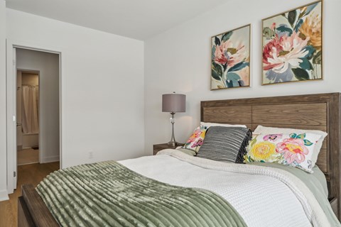 A bedroom with a bed, pillows, and two floral paintings on the wall.